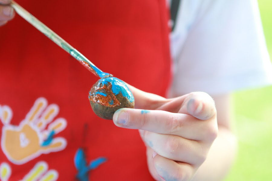 Kid painting small rock with blue paint