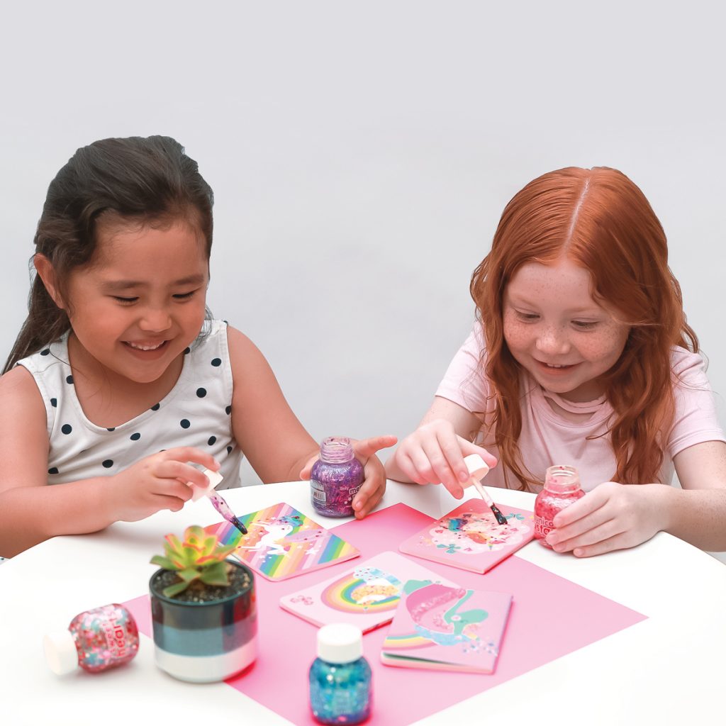 Two girls painting rainbows and unicorns with Pixie Paste Brush-On Glitter Glue