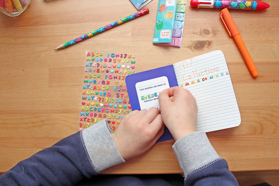 Kid putting together journal with alphabet stickers onto a pocket notebook