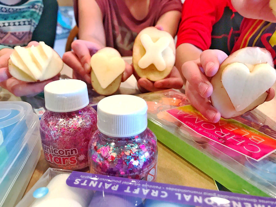 Kids holding up DIY Valentine's potato stamps with OOLY products at their side