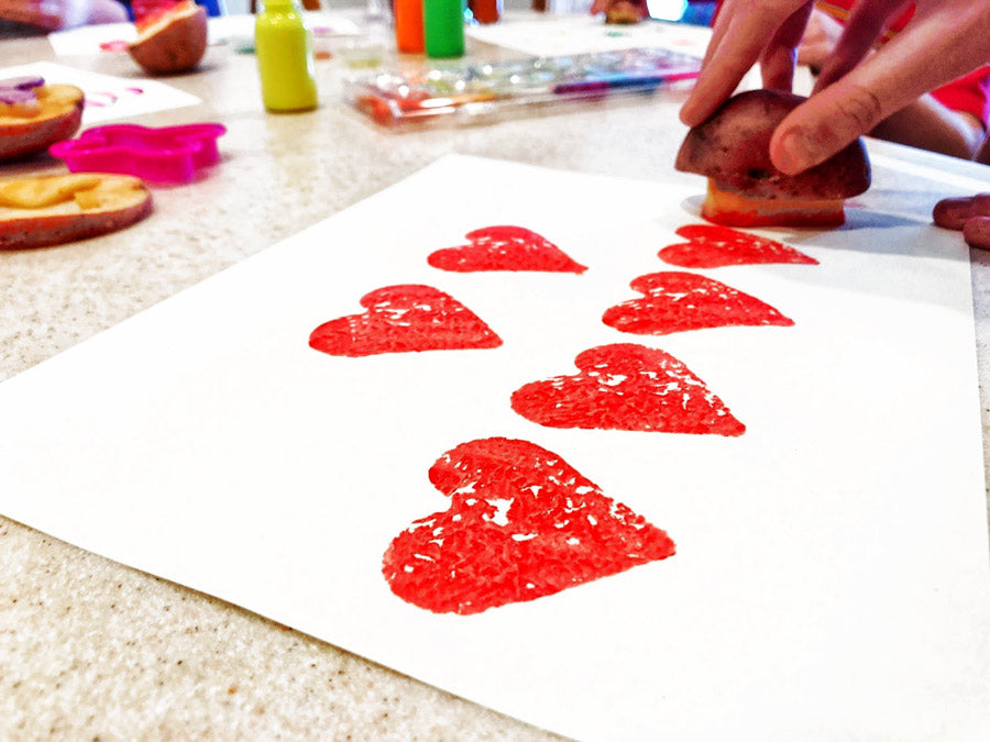 Stamping hearts on paper with DIY potato stamp for Valentine's Day