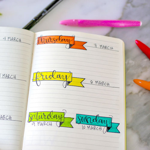 Weekly planner in colored bullet journal with markers and pens