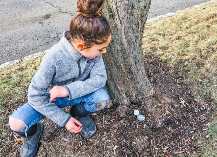 Girl leaving rocks painted with positive messages under tree