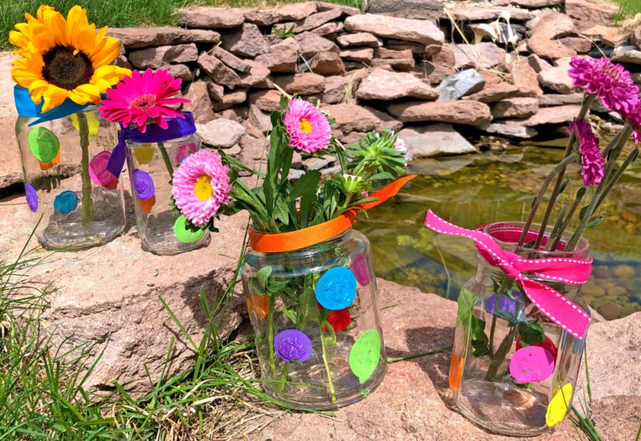 Painted DIY flower vases made with recycled mason jars next to a pond