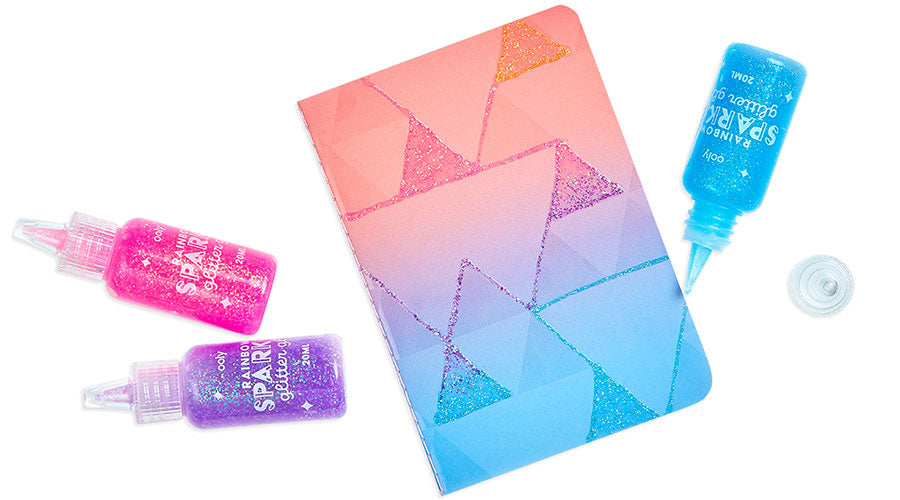 pink, purple and blue glitter glue with pink and blue journal on white surface