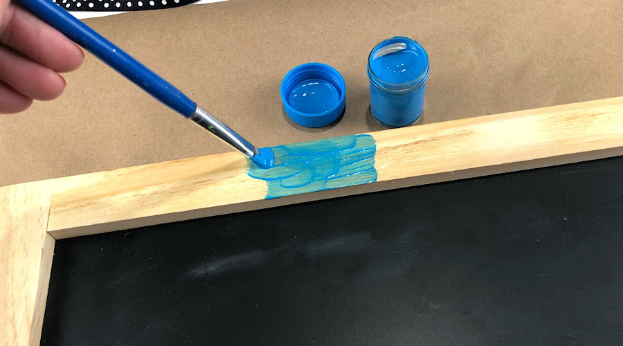 hand using blue paintbrush to paint wooden frame with blue paint
