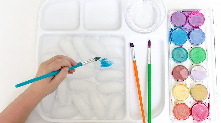 child hand holding blue paint brush, painting ice cubes on tray