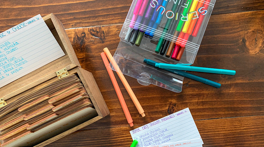 wooden card holder, colorful pens and index card on wooden surface