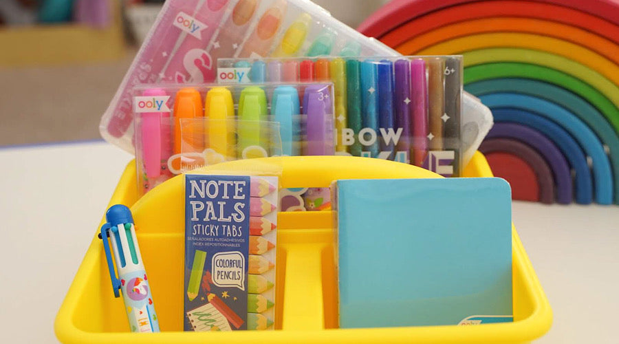 colorful school supplies in yellow bin with rainbow in background