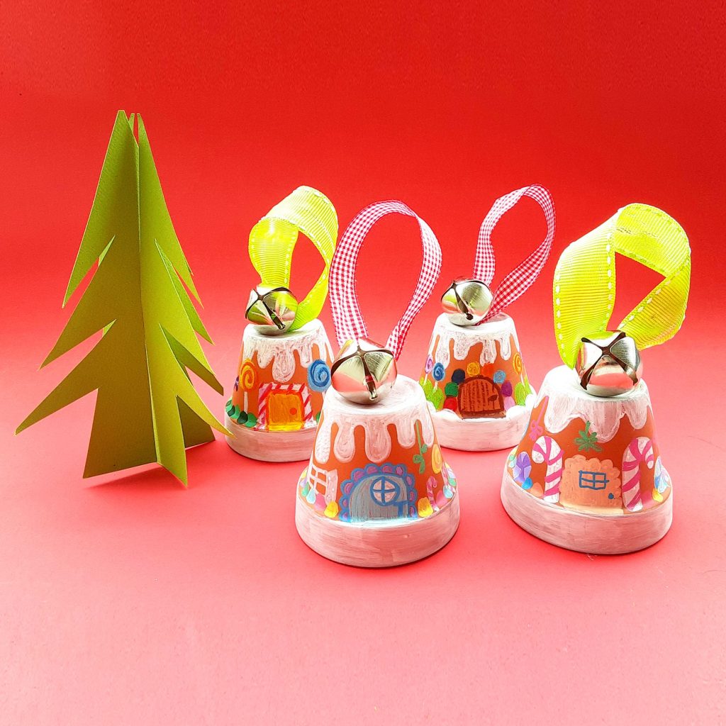 Terracotta gingerbread house christmas tree ornaments next to paper christmas tree on red background
