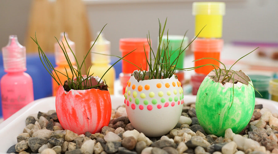 decorated egg shells on gravel with grass growing in them