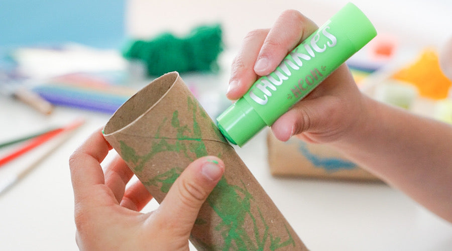 hand holding green chunkies paint stick coloring on toilet paper roll