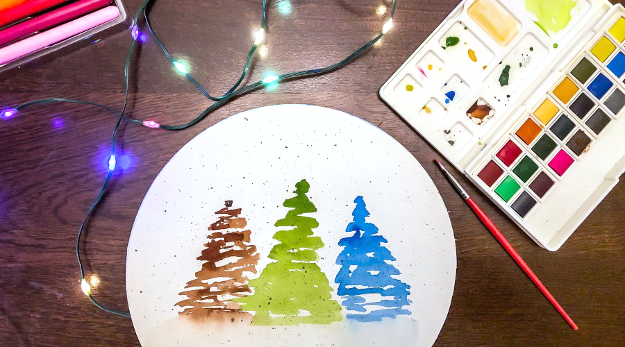 brown, green and blue trees on white paper on brown surface surrounded by lights and art supplies