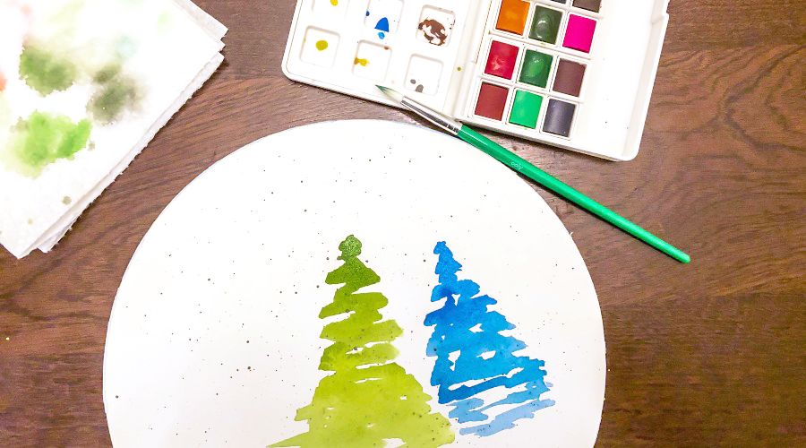 green and blue trees on white circular paper with art supplies on brown surface