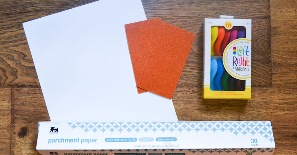 white paper, orange paper, parchment paper and crayons on wooden surface