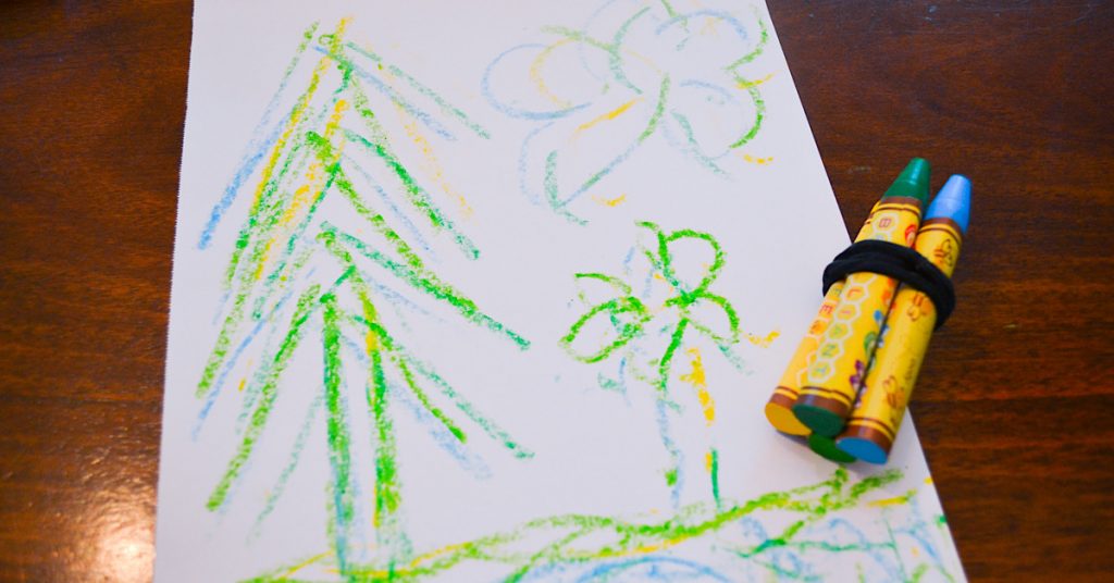 green trees on white paper with crayons tied together on wooden surface