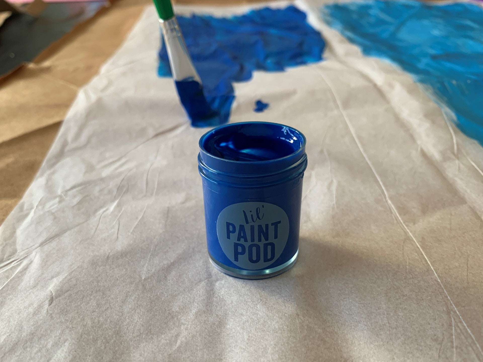 Opened ooly blue paint pods and paint brush painting tissue paper on a table