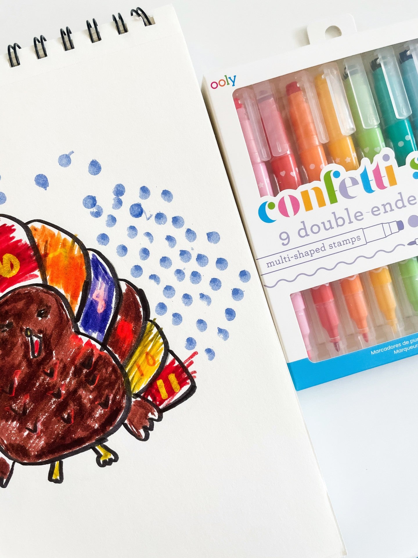 Sketchbook with colorful turkey drawing and confetti stamp markers on white table