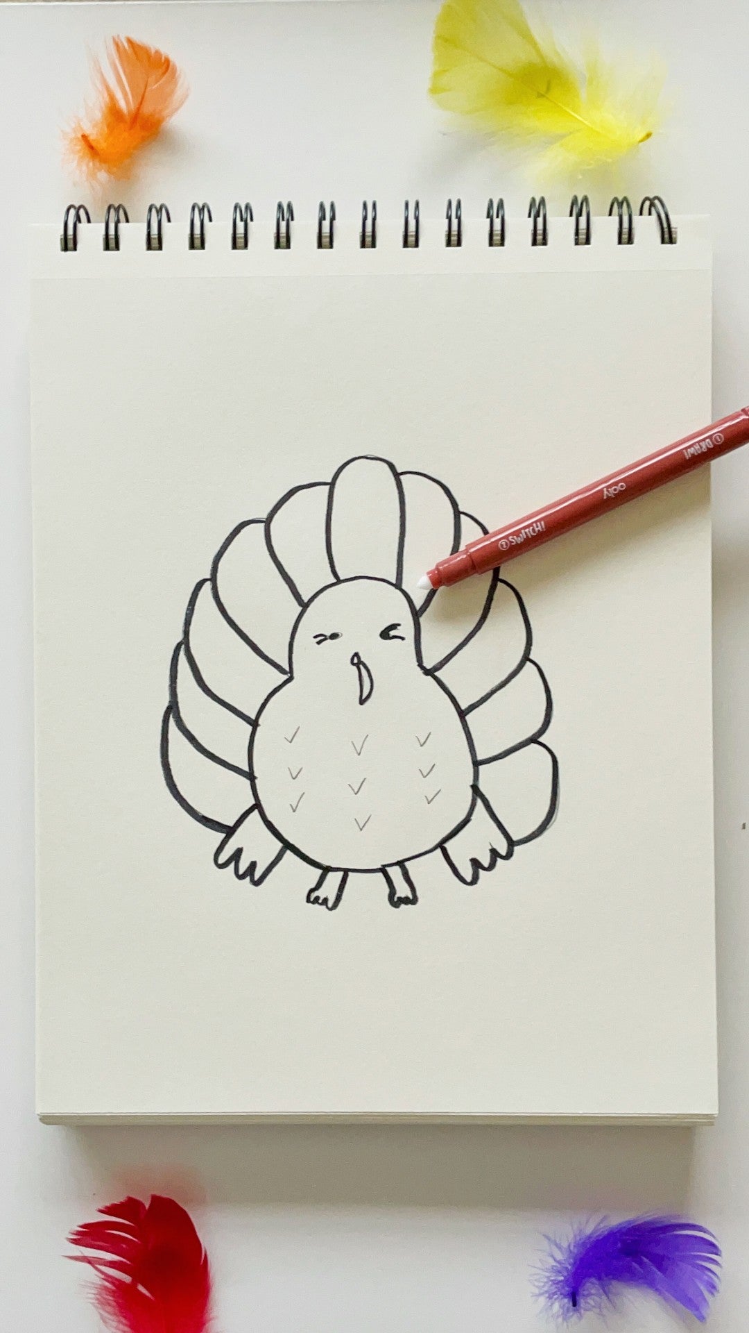 Sketchbook with marker on top of an outlined turkey with colorful feathers