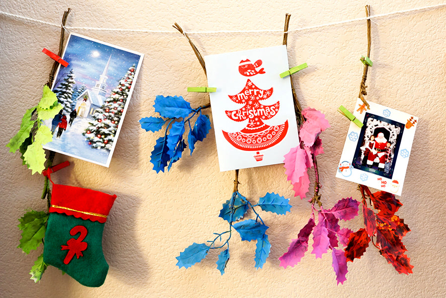 Christmas cards hanging on a string with colorful branches and leaves being held by clothes pins