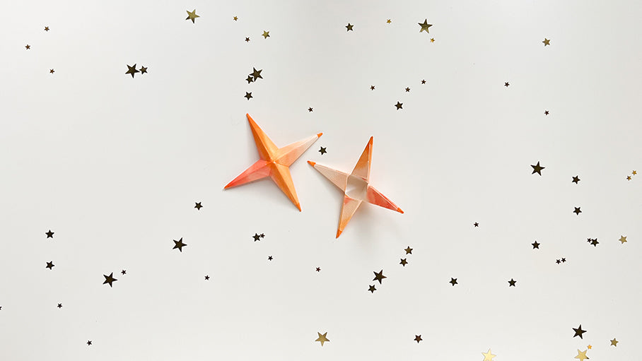 Two folded up paper stars colored orange on white table