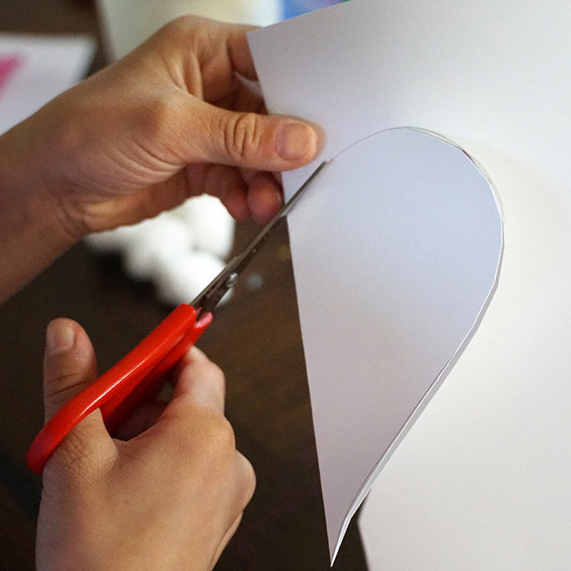 Hand using scissors to cut heart out of white sketchbook paper