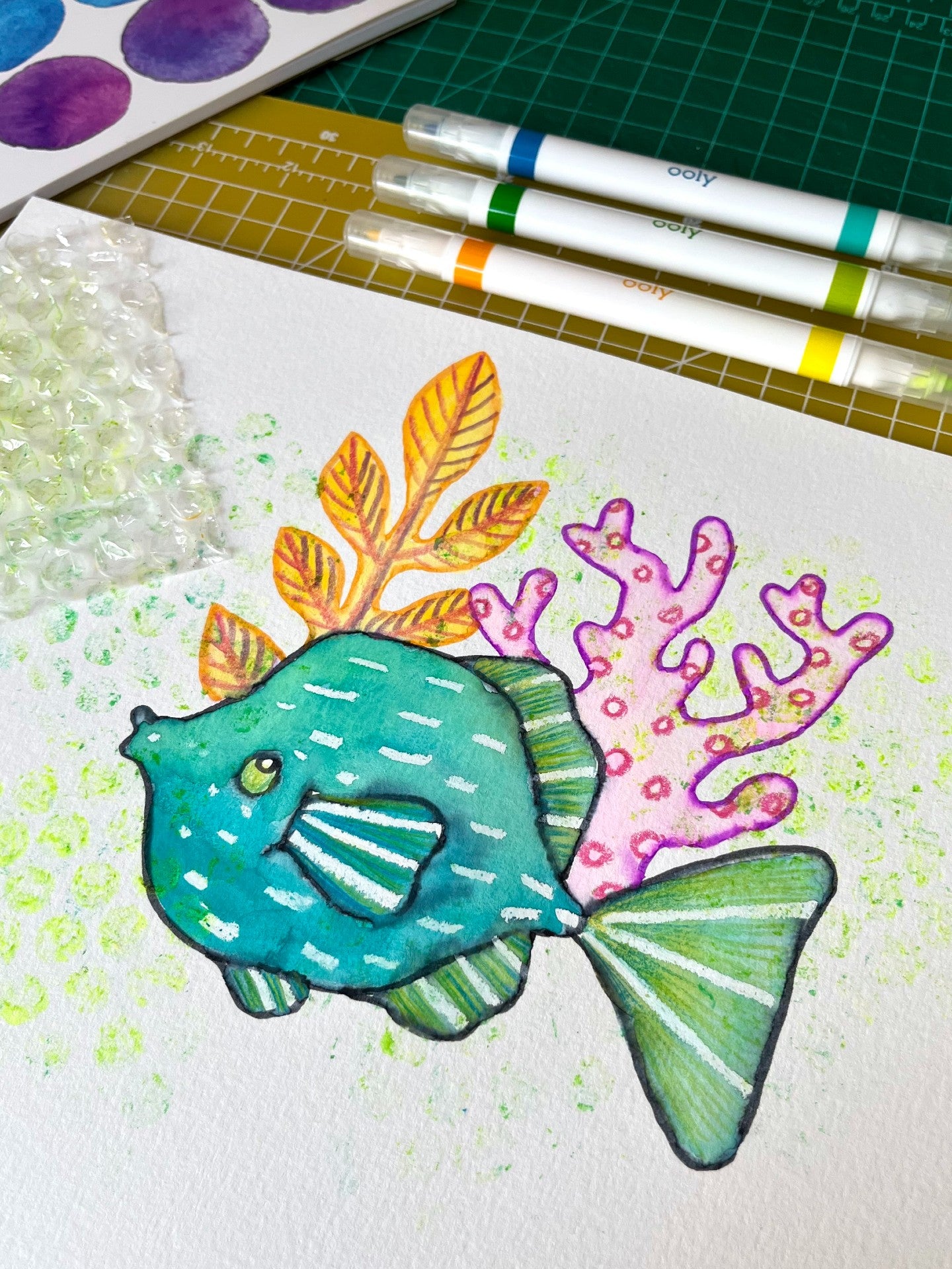 Colorful fish surrounded by coral on whitte paper with markers and bubble wrap