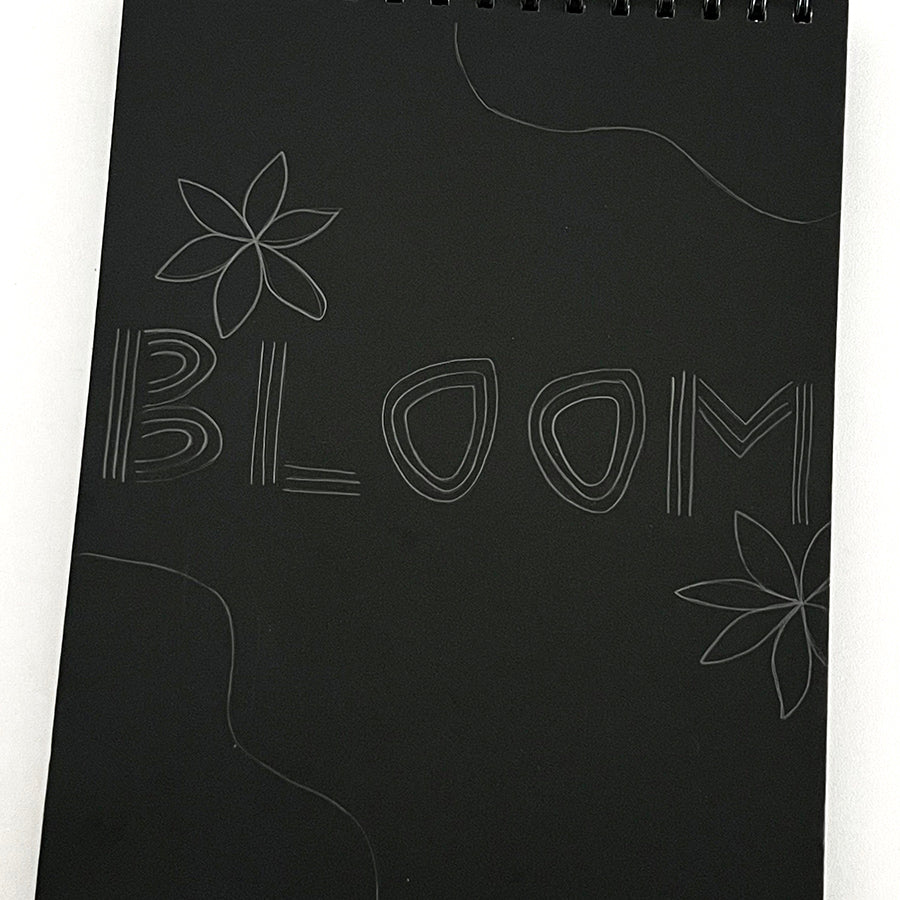 Black sketchbook with pencil designs of flowers and the word Bloom