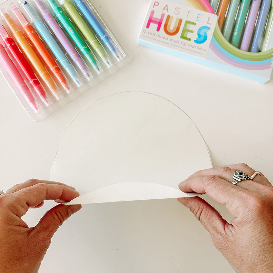 Person folding and flipping a white circle above art supplies on a white table