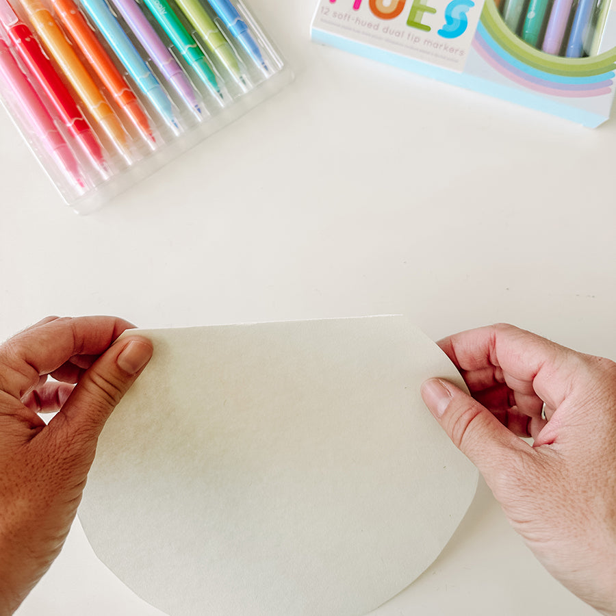 Person folding half inch paper circle above art supplies