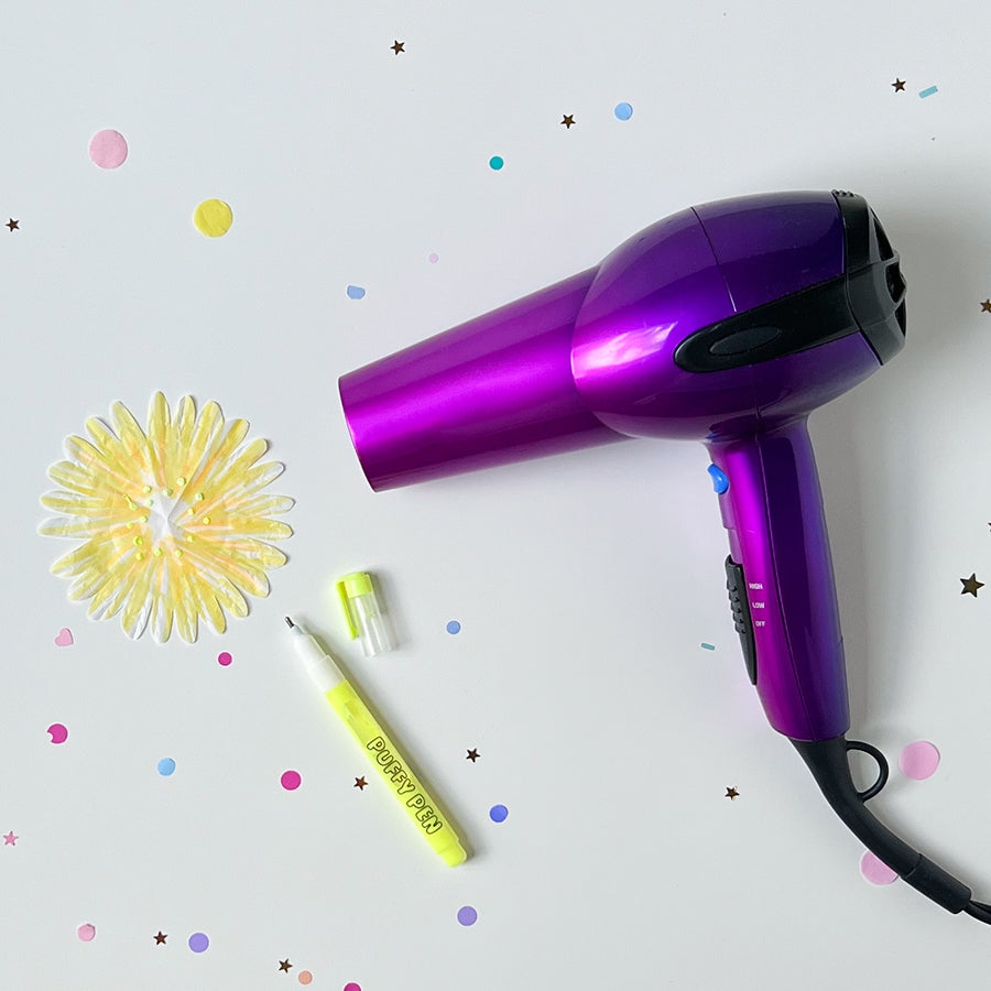 Hair blow dryer next to paper flower with puffy paint drying
