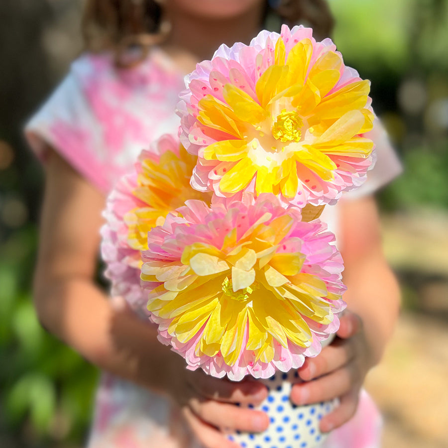 Little girl holding yellow and pink paper flower crafts outside
