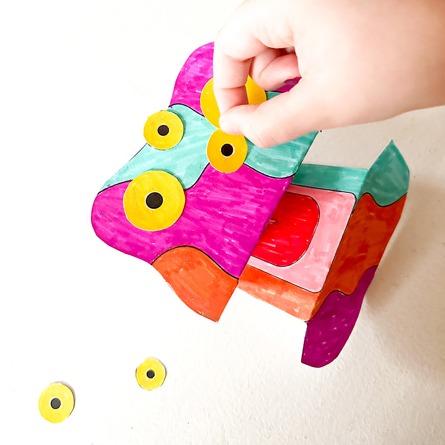 Hand gluing yellow cut out eyes colorful folded up paper craft