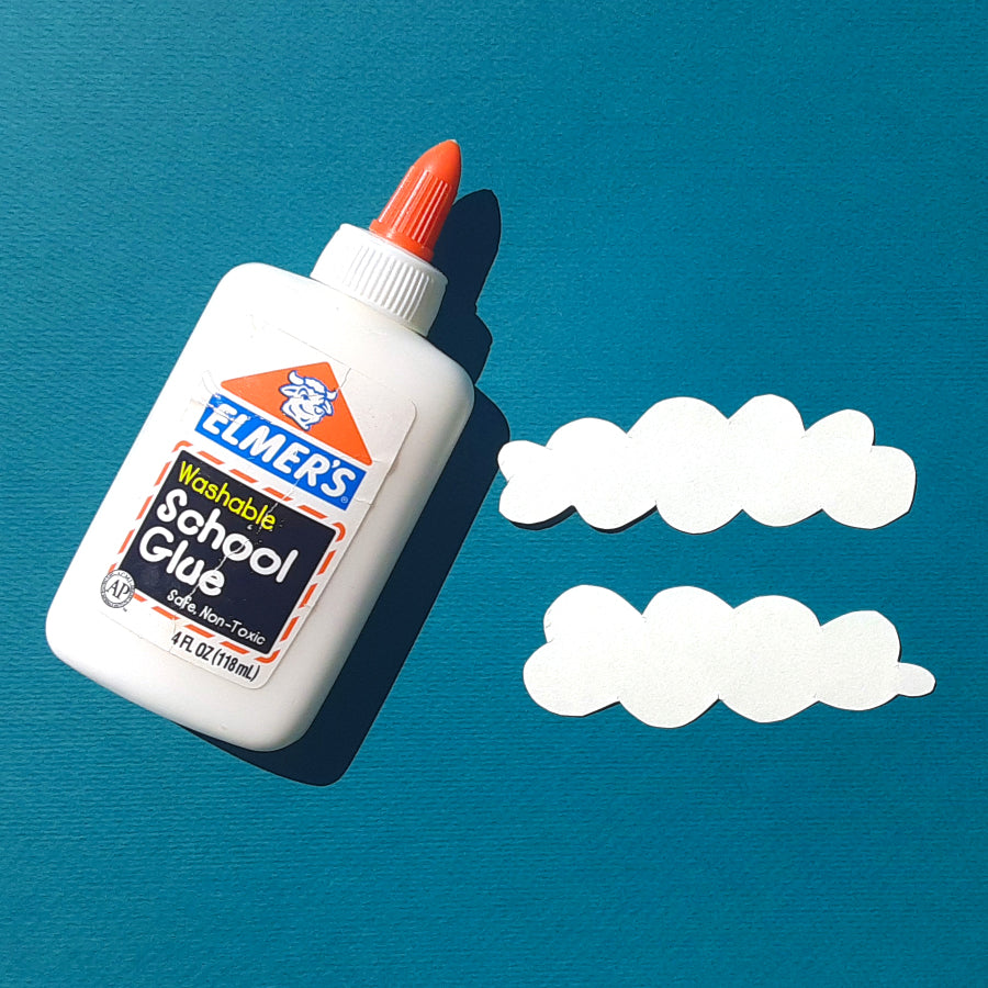 Elmer's glue on a blue surface with sketchbook paper cut in the shape of clouds