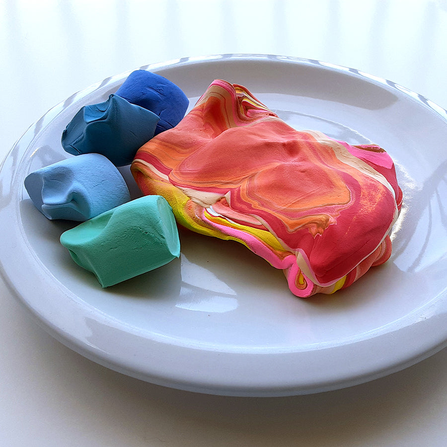 Green, blue, yellow, pink, and red clay on a white ceramic plate