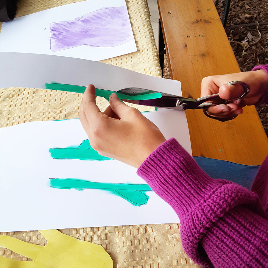 Kid in purple sweater cutting green flower stems out of sketchbook paper