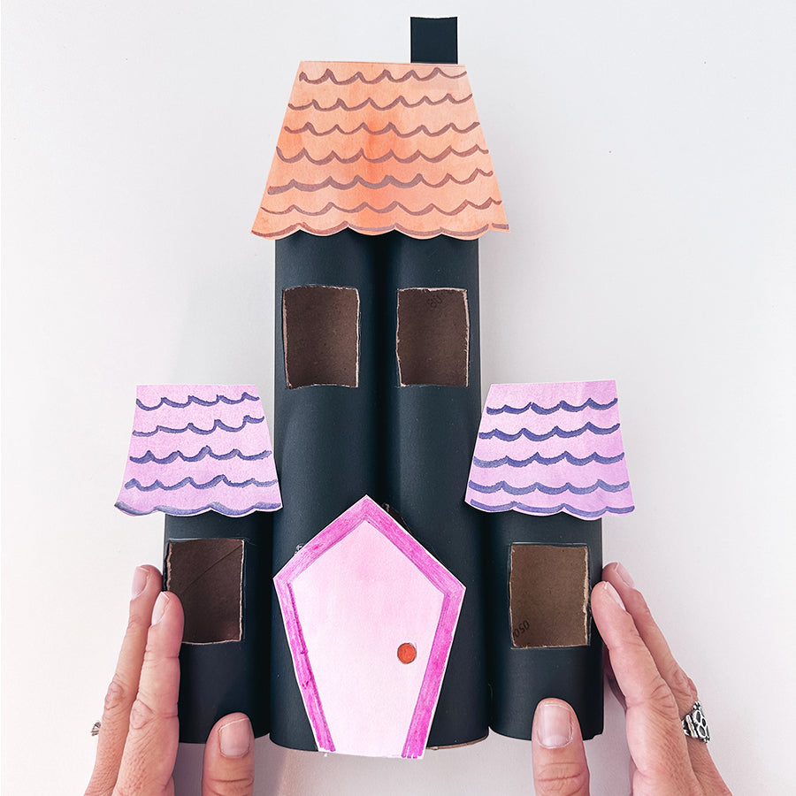 Hand holding haunted house craft with black, orange, purple and pink doors, windows and roof
