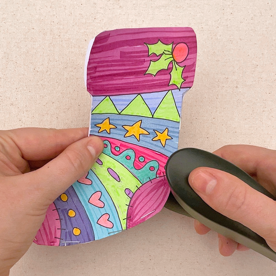 Hands using a stapler to staple two holiday socks back to back together