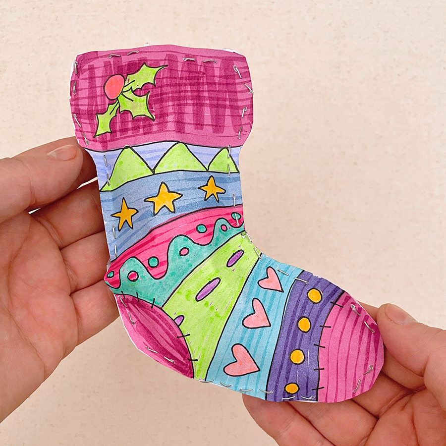 Hand holding finished Holiday sock with colorful lines, stars, hearts, mistletoe, and other shapes drawn on